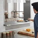 A man in a chef's uniform prepares food on a stainless steel pass-through shelf.