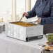 A woman in a chef's uniform serving food from a Galaxy countertop food warmer at a catering event.