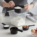 A person using OXO Good Grips black measuring cups to measure white powder in a bowl.