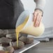 A person using an OXO Good Grips silicone measuring cup to pour yellow liquid.