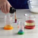 A person pouring yellow liquid into a red OXO beaker.