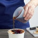 A person using an OXO Mini Squeeze & Pour measuring cup to pour brown liquid over a bowl of fruit.