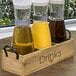 A wooden tray with glass jars of brown liquid and a Front of the House Drinkwise Carafe label.