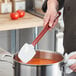 A person using a red Vollrath SoftSpoon to stir a pot of soup.