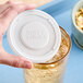 A hand holding a white plastic lid over a glass of liquid.