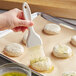 A hand using a Carlisle Sparta Spectrum pastry brush to spread butter on a round of white dough.