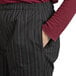 A person wearing Uncommon Chef red and white pinstripe chef pants with their hand in their pocket.