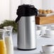 A Thermos Arc Cardinal glass insulated airpot on a table with a cup and saucer.