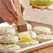 A person using a Thunder Group Nylon Bristle Pastry / Basting Brush to spread food on a tray.