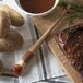 A Carlisle round pastry brush on a cutting board with a steak and potatoes.