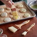 A person using a Carlisle Sparta boar bristle brush to spread white dough on a wooden surface.