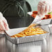 A hand in a white glove putting food into a Choice oblong foil container.