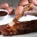 A person using a Carlisle boar bristle brush to baste meat on a table.