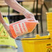 A gloved hand pouring Advantage Chemicals orange degreaser into a yellow bucket.