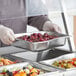 A person in a white coat holding a Vollrath stainless steel tray of food.