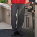 A man wearing Uncommon Chef black and gray houndstooth pants standing next to an outdoor grill.