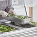 A Vollrath stainless steel long steam table pan with broccoli and onions inside.