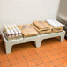 A Cambro solid top bow tie dunnage rack on a table with brown bags of food and a white bag with blue text on it.