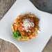 A white plate of pasta with Italian Style Seasoned Bread Crumbs on top served on a tile surface.