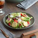 A plate of salad with lettuce, tomatoes, and other vegetables on an Acopa moss green matte coupe stoneware plate.