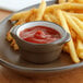 A plate of french fries with a sauce cup of ketchup on it.