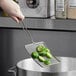 A hand holding a Tablecraft nickel mesh skimmer with brussels sprouts over a pot.