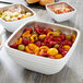 A Vollrath Pearl White metal serving bowl filled with food on a table.