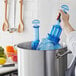 A person putting blue San Jamar Rapi-Kool bottles in a metal container of water.