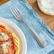 A Oneida New Rim stainless steel dinner fork next to a plate of spaghetti with sauce.