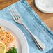 A Oneida New Rim stainless steel table fork next to a plate of food.