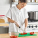 A woman in a white Uncommon Chef cook shirt cutting vegetables on a cutting board.