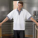 A man wearing a white Uncommon Chef cook shirt with Shepherd's Check trim standing in a room.