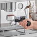 A hand holding an Estella Caffe One Group Automatic Espresso Machine over a counter.