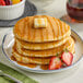 A stack of Krusteaz sweet cream pancakes with syrup and strawberries on top.
