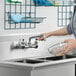 A woman using a Waterloo wall-mounted faucet to wash dishes in a sink.