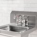 A stainless steel deck-mounted faucet with 4-inch centers and a 6-inch swing spout installed on a metal sink.
