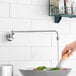 A woman using an Emperor's Select Wok Range Faucet to wash vegetables in a bowl.