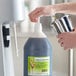 A person pouring I. Rice vanilla milkshake syrup into a large container on a counter.