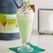 A glass of a green mint milkshake with a bottle of I. Rice Mint Milkshake Base syrup on the side.