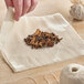A hand holding Monarch Brands unbleached cheesecloth with a pile of spices.