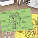 A green Oxford index card with a drawing of a heart on it on a table with a phone and notepad.