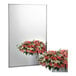 A Bobrick wall-mounted mirror reflecting a white vase with pink and white roses.