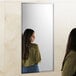 A woman with long brown hair leaning against a Bobrick wall-mounted mirror.