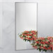 A Bobrick wall-mounted mirror reflecting a vase of flowers.