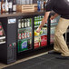 A man opening an Avantco black narrow sliding glass door back bar refrigerator.