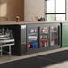 An Avantco back bar refrigerator with a galvanized top and glass sliding doors filled with drinks on a counter.