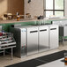 An Avantco stainless steel back bar with bottles on a metal shelf.