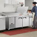 A chef preparing food in a commercial kitchen at an Avantco 3 door refrigerated pizza prep table.