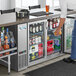 A man standing at a bar with an Avantco back bar refrigerator full of drinks.