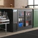 An Avantco back bar cooler with bottles of beer on metal shelves.